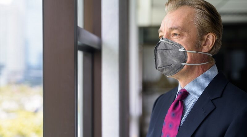 Mature businessman thinking and looking outside the window with mask for protection from corona virus outbreak